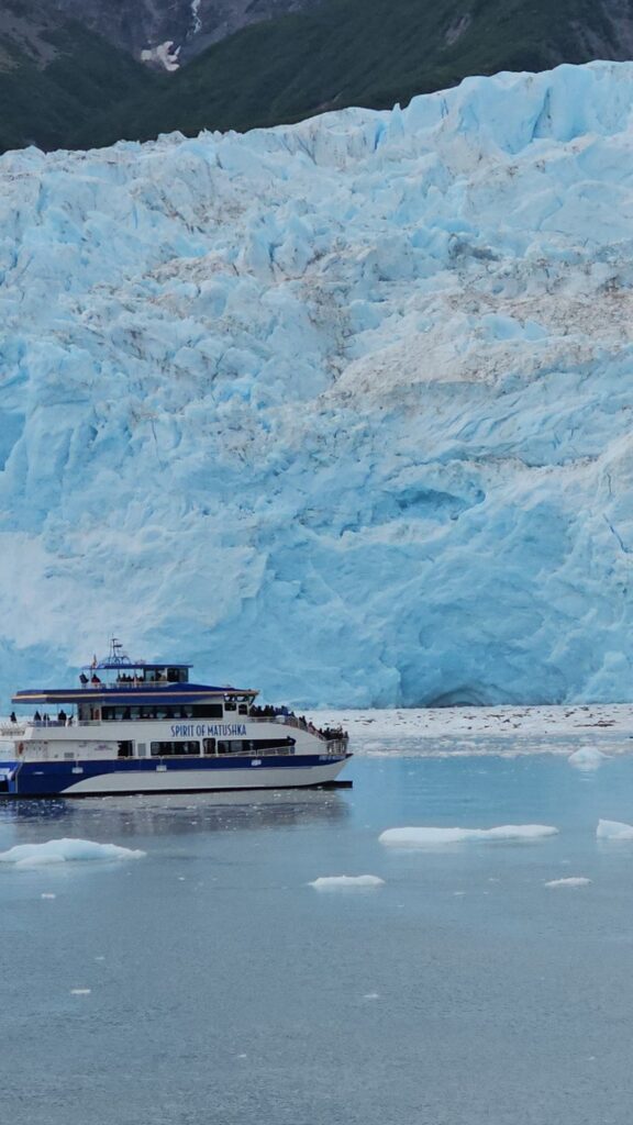 Cruise boat sailing near a massive blue glacier in Alaska surrounded by icy waters and mountain scenery